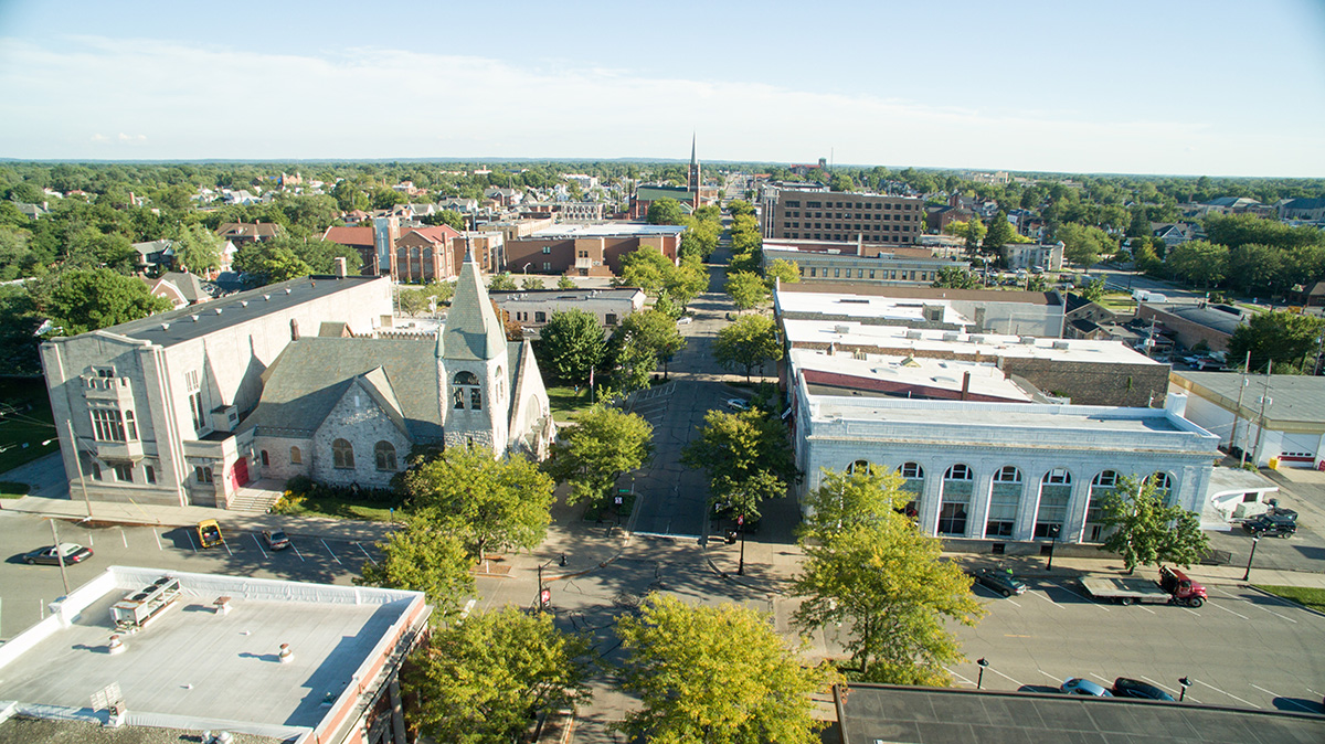 Aerial view of downtown Michigan City, Indiana showing historic churches, commercial buildings, and treetops.