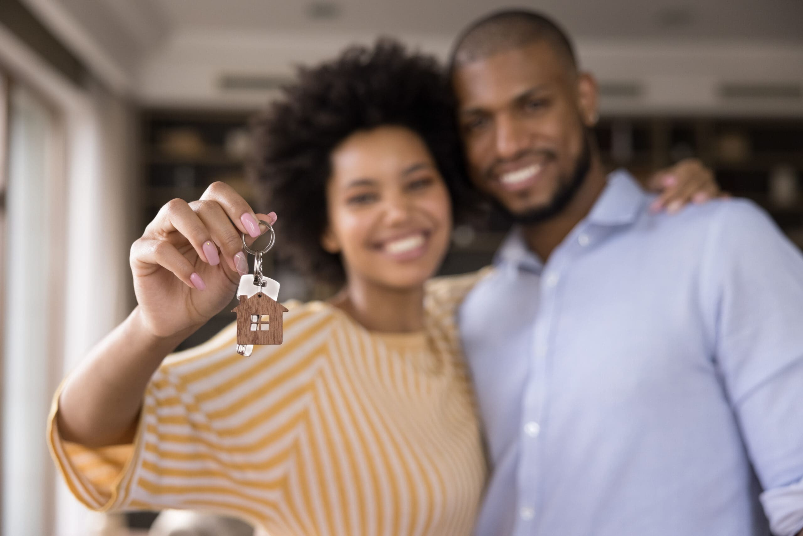 Happy couple holding a house key with a wooden home-shaped keychain, celebrating new housing opportunity.